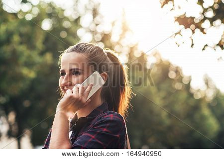 Attractive young brunette woman smiling and talking on a cellphone while walking alone outside