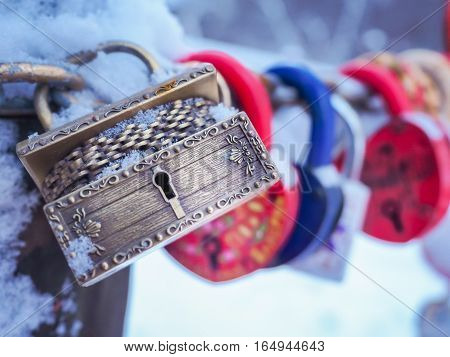 Golden padlock in the shape of a chest with many other locks hanging on a chain outdoors in winter. Valentine's Day Concept