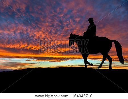Silhouette of a rider on her horse on top of a mountain with dramatic sunset in the background. Copy space.