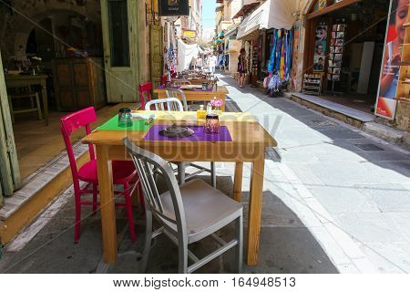 Rethymnon, Island Crete, Greece - June 23, 2016: Tables and chairs of cafe are on the narrow street of Rethymnon (part of Old Town)