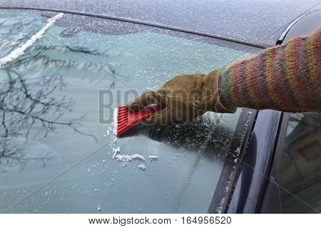 Winter scene human hand in glove scraping ice from windshield of car