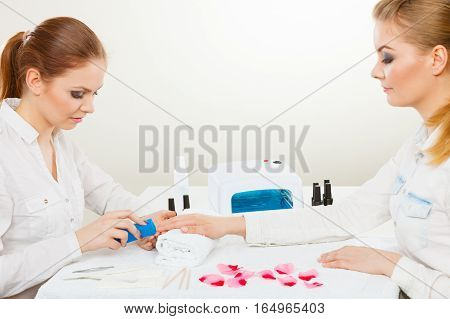 Relaxing time and wellness day concept. Blonde elegant woman visiting professional manicurist salon. Beautician makes perfect nails to client.