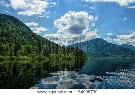 expanse of water with the reflection of clouds between the mountains. On the banks of growing forest