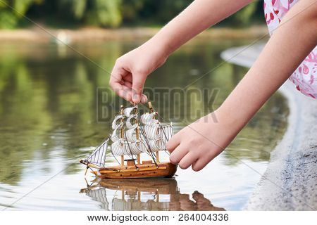 girl playing with a toy sailing ship by the river, hand closeup