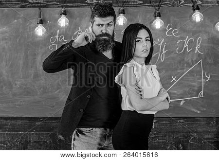 Man With Beard And Sexy Girl Teacher Stand In Classroom, Chalkboard On Background. Teacher And Stric
