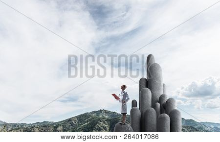 Young Female Doctor With Folder In Hands Satnding On Stone Column