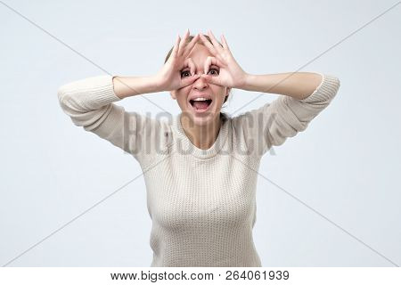 Pretty Girl With Surprised Face Holding Fingers Near Eyes Like Glasses. Mask Like Super Hero Or Owl