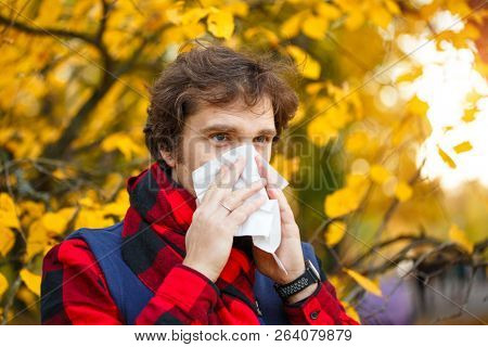 Man with cold rhinitis on autumn background. Fall flu season. Ill sick sneezing male. Handkerchief, vaccine against influenza virus Caught Cold Headache Allergy runny nose