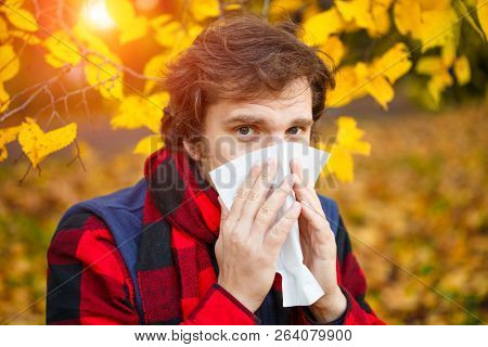 Man with cold rhinitis on autumn background. Fall flu season. Ill sick sneezing male. Handkerchief, vaccine against influenza virus Caught Cold Headache Allergy runny nose