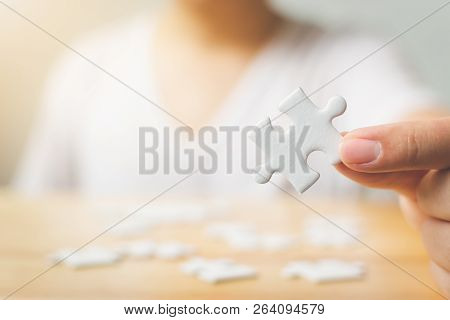 Hand Of Male Trying To Connect Pieces Of White Jigsaw Puzzle On Wooden Table. Healthcare For Alzheim