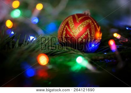 New Year's Toy - A Golden Ball Lies On A Tree Branch Among Colorful Lights.