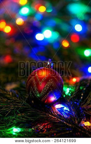New Year's Toy - A Red Golden Ball Lies On A Tree Branch Among The Multicolored Lights.