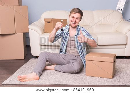 New Home, Real Estate Owner And Moving Concept - Young Man Holding Keys Of New Home And Showing Thum