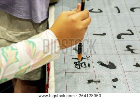 Closeup Hand Of Person Holding Chinese Brush And Demonstration Chinese Letters On Fabric.