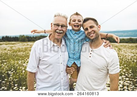 Grandfather And Son Spending Time With Little Child During The Sunset.
