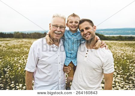 Grandfather And Son Spending Time With Little Child During The Sunset.