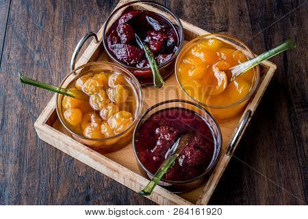 Various Glass Bowl Of Fruit Jams Apricot, Cherry, Strawberry, Damson Plum In Wooden Tray.