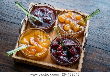 Various Glass Bowl Of Fruit Jams Apricot, Cherry, Strawberry, Damson Plum In Wooden Tray.