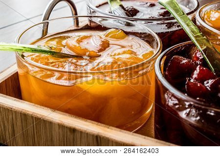 Various Glass Bowl Of Fruit Jams Apricot, Cherry, Strawberry, Damson Plum In Wooden Tray. Breakfats 