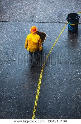 New York, Usa - May 03, 2016: Construction Worker In A Yellow Protective Cloak Pushing A Wheelbarrow