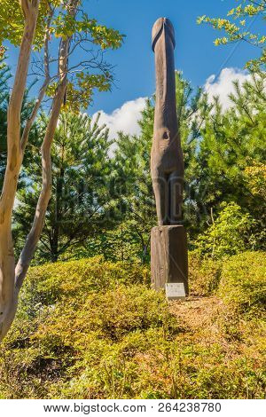 Samcheok, South Korea; September 25, 2018: Wooden Statue Of Human Penis Standing In Front Of Green F