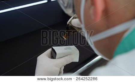 A Young Professional Master Holds A Jar In A White Coat, Safety Goggles, White Rubber Gloves.