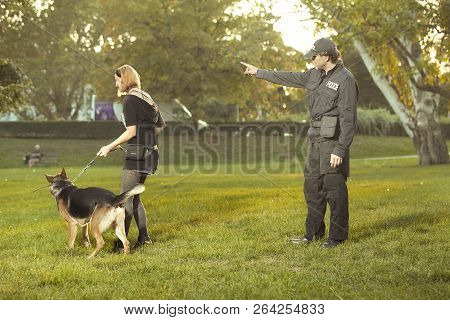 Policeman In Uniform Checking Lady With German Shepherd In City Park