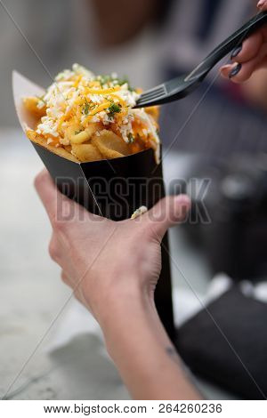 Closeup Of Hand Holding Fries With Cheddar Cheese, White Cheee And Dip While Sticking The Fork In. T