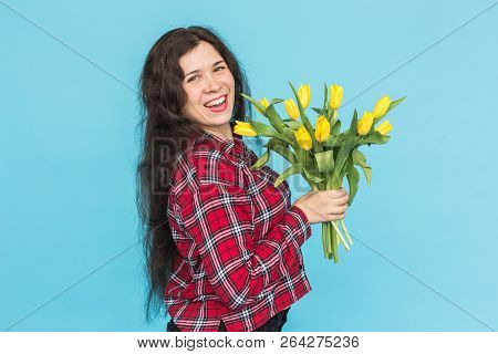 Laughing Young Caucasian Woman With Bouquet Of Tulips On Blue Background.