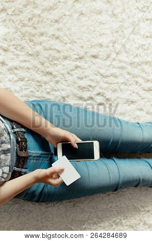 Young Woman Holding Credit Card And Using Phone Sitting On Floor. Payment.  Online Shopping Concept.