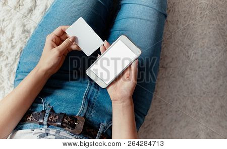 Young Woman Holding Credit Card And Using Phone Sitting On Floor. Payment.  Online Shopping Concept.