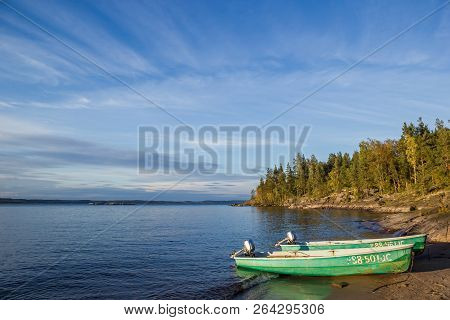 Blue Sky Above Water And Beach At  Lake With Two Green Pella Boats