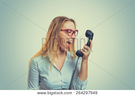 Young Woman In Glasses Holding Telephone Receiver And Yelling With Anger