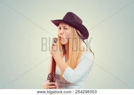 Modern Blond Woman In Cowboy Hat Holding Gun And Blowing At It After Shooting