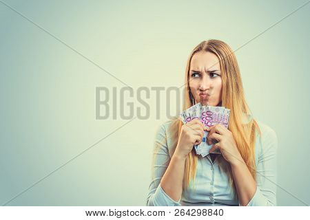 Blond Woman In White Shirt Holding Heap Of Money And Frowning In Greediness Looking Away