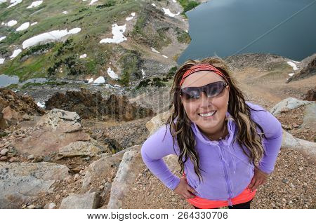 Attractive Woman Wearing Sunglasses Poses Near An Alpine Lake Along The Beartooth Highway In Montana