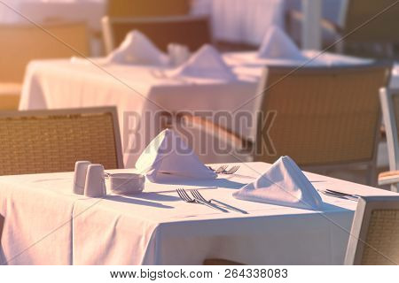 Chairs And Tables At Sunset At Hotel Restaurant. Cutlery And Napkings On Tables.