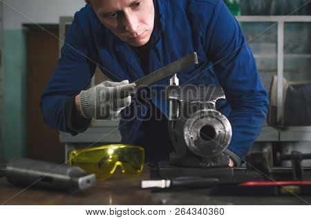 Man Worker Is Working With Iron Detail On Vise Grip On Blacksmith Table And Using A File.