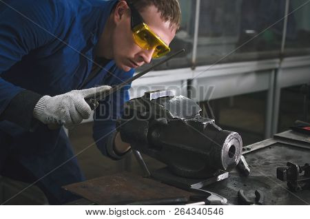 Man Worker Is Working With Iron Detail On Vise Grip On Blacksmith Table And Using A File.
