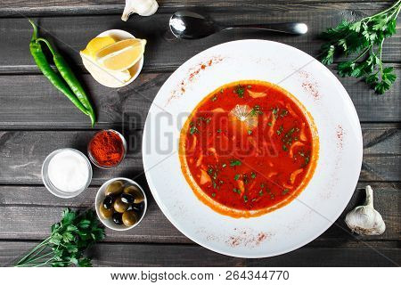 Soup With Meat, Olives, Herbs And Lemon In Plate, Served With Sour Cream, Peppers On Dark Wooden Bac