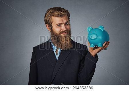 Portrait Of Young Bearded Hipster Businessman Man Holding A Piggy Bank Against A Gray Grunge Studio 