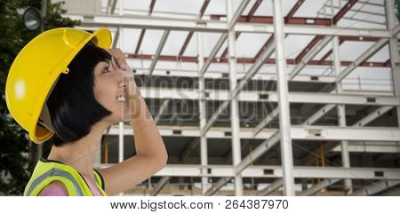 Female architect in hard hat looking away against white background against metallic scafolding on building
