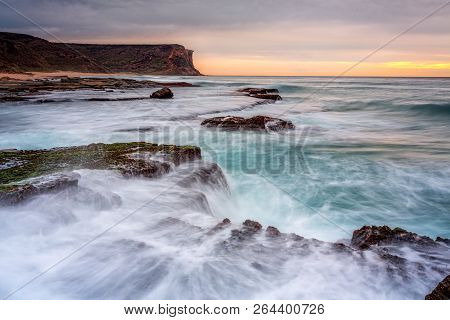 Coastal Sunrise With Soft Cloud Cover And Waves Breaking Over Exposed Rocks Bearing Cunjevoi And Oth