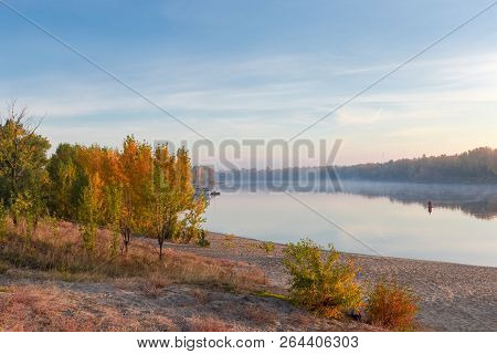 Section Of The Plain River With Sandy Bank And Trees With Autumn Leaves On A Foreground, Fog Over Wa