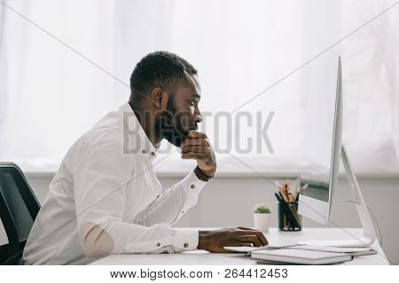 Side View Of Handsome African American Businessman Resting Chin On Hand And Working At Computer In O