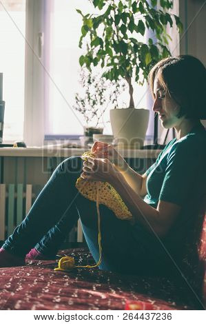 Girl Knits Crochet At Home. Woman Engaged In Needlework. A Knitter Sits On A Sofa And Works. Creativ