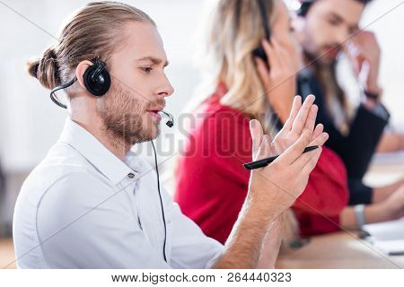 Selective Focus Of Call Center Operators In Headsets With Notebooks Working At Workplace In Office