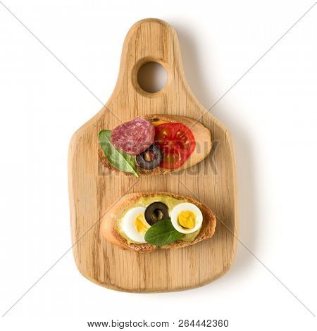 Open faced sandwich canape or crostini on a wooden serving board isolated on white background closeup. Top view.