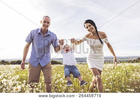 Parent Walking With Her Baby Son On Daisy Field At The Sunset Time