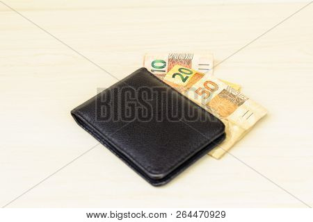 Black Wallet Closed With Some Notes Of Brazilian Money, The Real One. Light Background